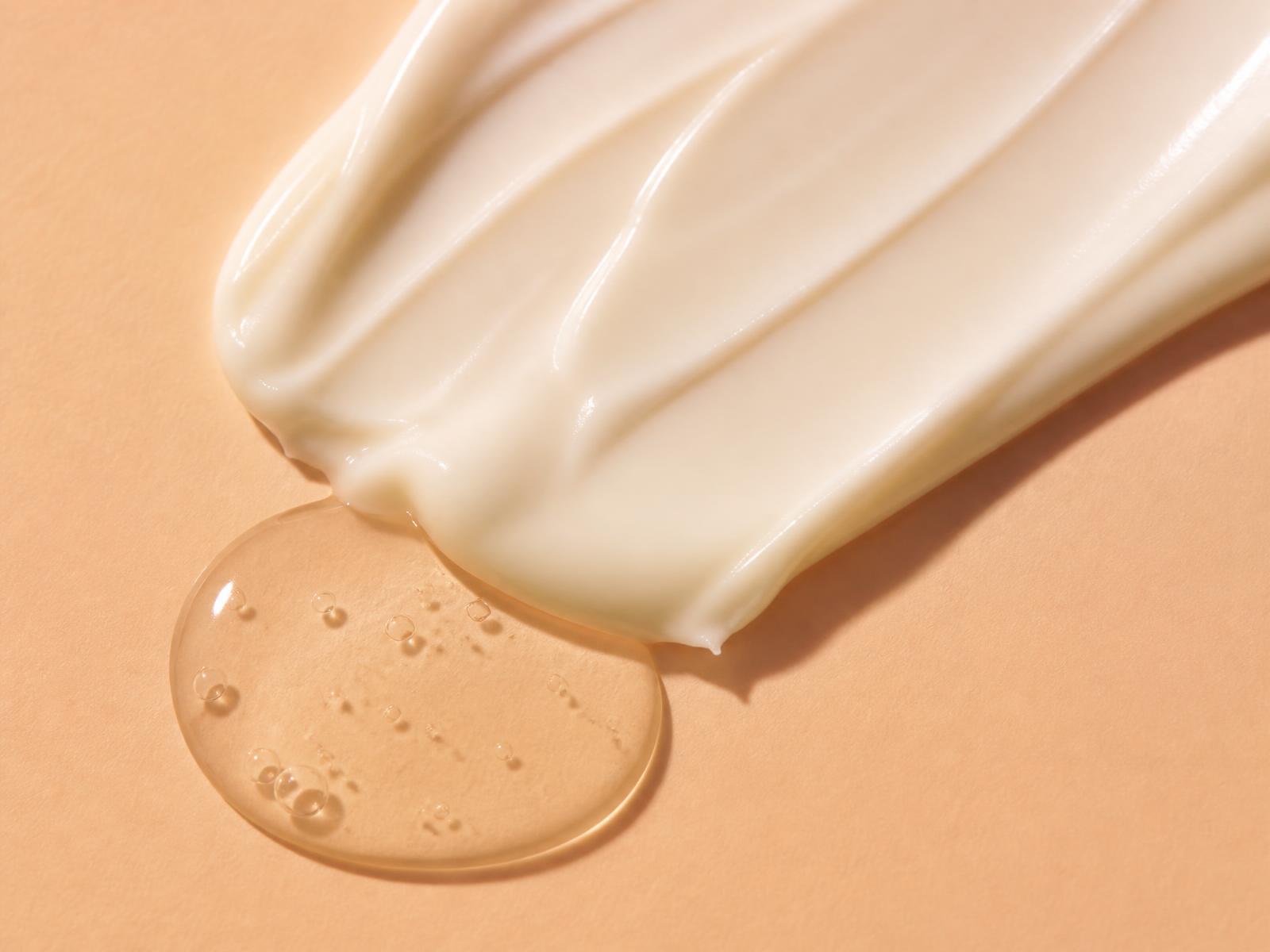 Macro swatch of cream and serum on a peach surface