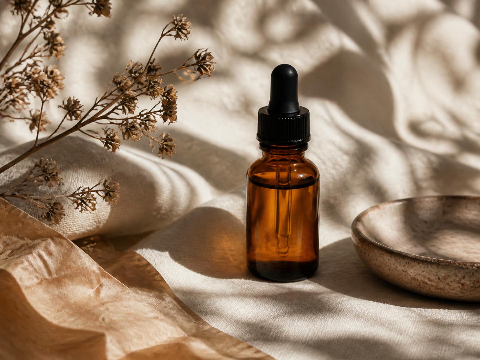 Warm editorial still life of an unbranded dropper bottle and ceramic dish on linen